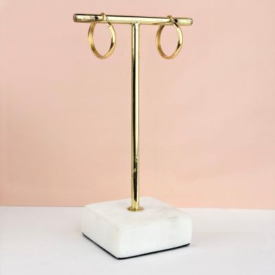 un socle en marbre blanc sur lequel sont posées deux boucles d'oreilles en forme d'anneaux dorés