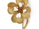 une image représentant une broche en forme de fleur en or, ornée d'une pierre violette en son centre