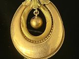 an image of a gold pendant with a pearl hanging from it ' s center