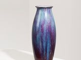 purple and blue vase sitting on a white pedestal in a white room