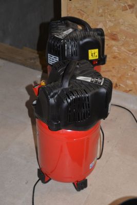 a red air compressor sitting on the floor next to a black and white dog