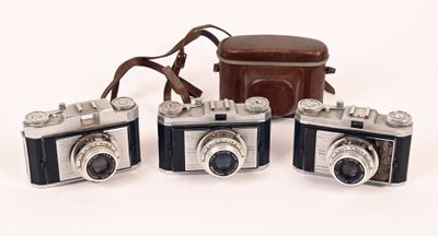 three old cameras are sitting next to each other on a white surface