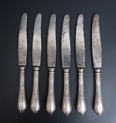 six couteaux argentés sont alignés sur une surface noire