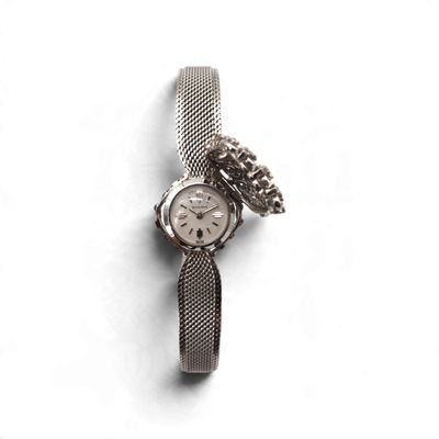une montre en argent, entourée d'une chaîne, posée sur une surface blanche