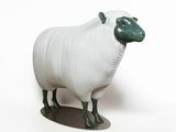 une figurine de mouton blanche et verte posée sur une surface blanche