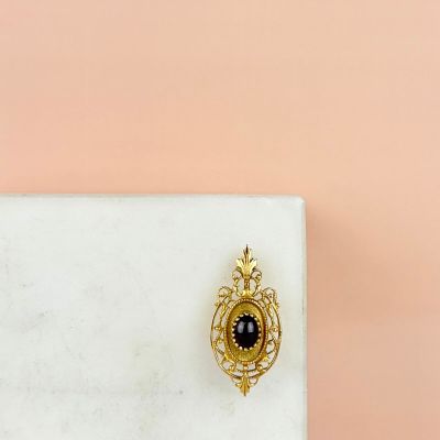 une image représentant une broche dorée et noire posée sur une surface en marbre