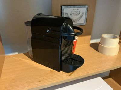 a black coffee maker on a wooden shelf next to a roll of tape