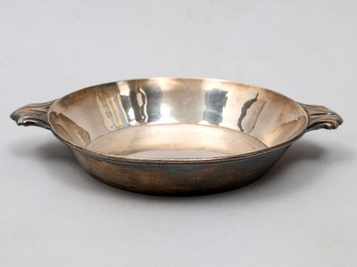 une assiette en argent antique avec une poignée sur une surface blanche