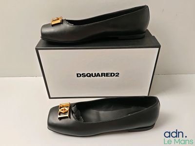 Des chaussures en cuir noir ornées de boucles dorées sont exposées devant une boîte