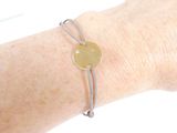 a woman ' s arm with a bracelet with a gold disc on it