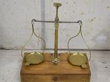 une vieille balance en laiton avec un socle en bois sur lequel reposent deux plateaux en laiton