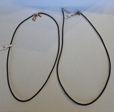 deux colliers en cuir noir avec des fermoirs en argent, posés sur une surface blanche