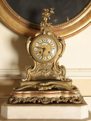 a gold clock sitting on a marble base in front of a mirror