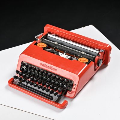 une machine à écrire rouge posée sur une feuille de papier blanche