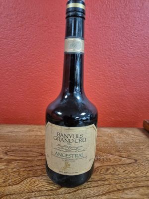 an old bottle of brandy sits on a wooden table in front of a red wall