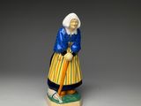 an old figurine of a woman with a cane sitting on top of a table