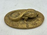 plaque en laiton surmontée d'un lézard, posée sur un fond blanc