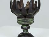 a metal vase with a flower on it on a white surface