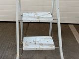 un tabouret en métal blanc devant un mur blanc