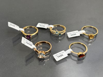 six bagues différentes, munies d'étiquettes, posées sur une table