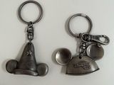 On voit deux porte-clés métalliques à l'effigie de Mickey Mouse posés sur une surface blanche.