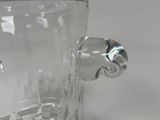 a clear glass vase with a metal handle on a table