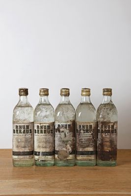 six vieilles bouteilles de gin posées sur une table en bois, avec un mur blanc en arrière-plan
