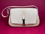 a white purse with a metal handle on a pink background