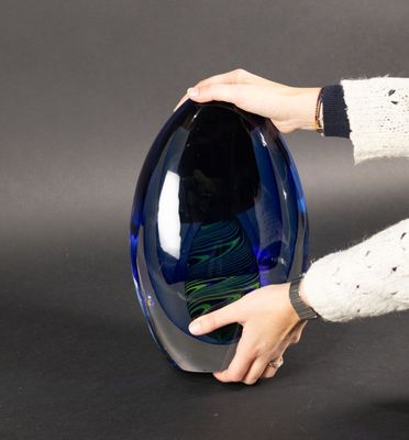 une personne tenant un vase en verre bleu posé sur une surface noire