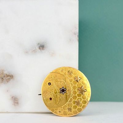 broche plaquée or ornée de pierres noires et blanches sur un fond en marbre