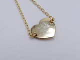 a close up of a gold heart necklace on a white surface