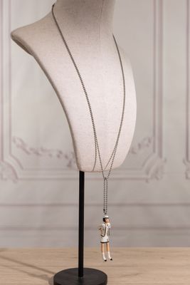 a white mannequin with a silver necklace on a black stand