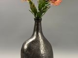 un vase noir avec des fleurs orange à l'intérieur, posé sur une table
