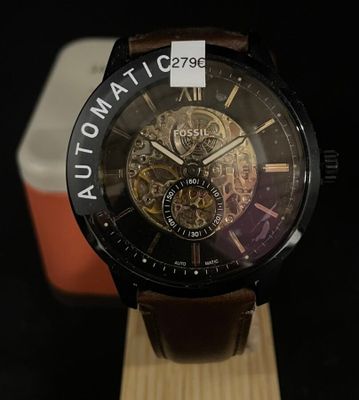La montre est posée sur un socle en bois, avec une boîte en arrière-plan.