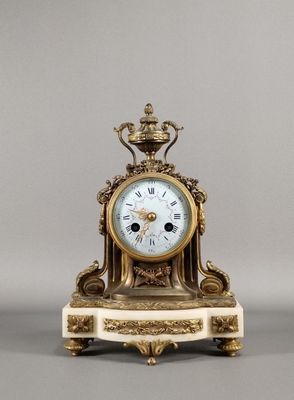 une horloge dorée et blanche posée sur un socle, surmontée d'une couronne