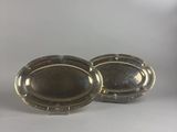 two silver oval trays with handles on a white surface