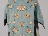 an old blue jacket with flowers and birds on it on a mannequin stand