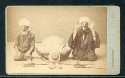 une vieille photo montrant deux hommes assis par terre avec un gros animal