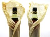 two bottles of wine wrapped in paper on a table