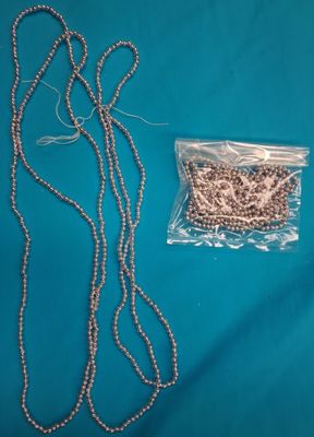 a close up of a necklace and a bag of beads on a blue surface