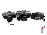 three cameras are lined up on a white surface with a camera strap around them