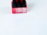 trois bouteilles de Coca-Cola dans une boîte rouge posée sur une surface blanche