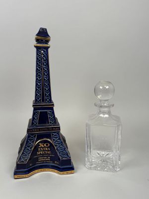 un flacon de parfum en forme de Tour Eiffel bleu et or à côté d'un flacon en verre transparent
