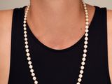 une femme vêtue d'un débardeur noir et d'un collier de perles