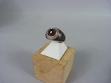 bague en argent massif sertie de grenatite et de diamants, posée sur un socle en bois