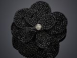 une broche en forme de fleur, composée de perles noires et ornée d'un diamant au centre