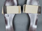 pair of women ' s silver sandals with beige straps on a gray surface