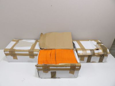 trois cartons contenant des t-shirts orange, posés sur une table