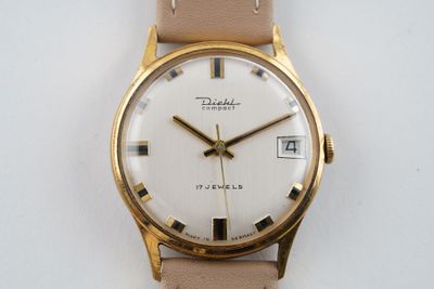 une montre-bracelet en or avec un cadran blanc sur un bracelet beige