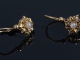 a pair of gold earrings with pearls on them on a black surface